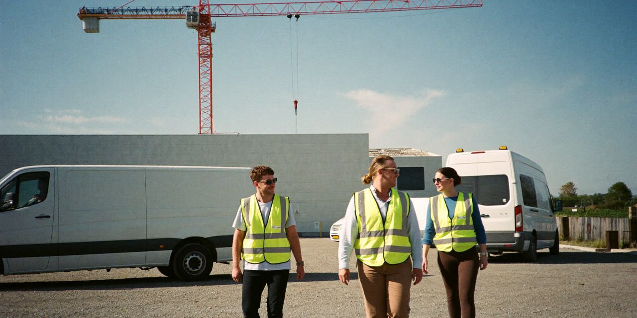 Technici in gele hesjes lopen over een grindterrein van witte bussen naar een datacenter in aanbouw