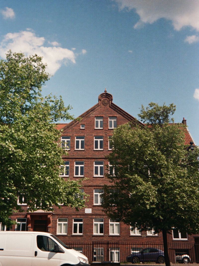 Appartementengebouw van rode baksteen in een straat met bomen, met een witte bus ervoor
